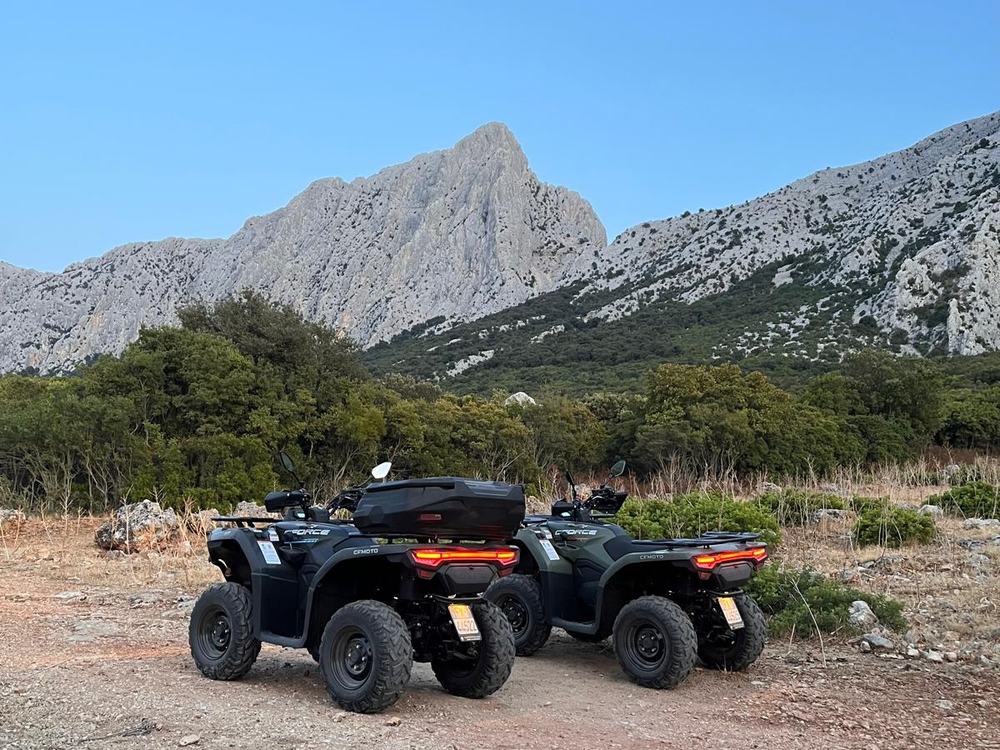 Due quad CFMOTO Force, uno nero e uno verde, su uno sterrato tra la macchia sotto una cima calcarea appuntita