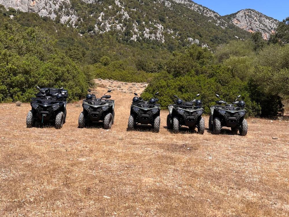 Cinque quad verde scuro di Zola's Quad Experience con caschi sui sedili, in un prato secco sotto monti calcarei